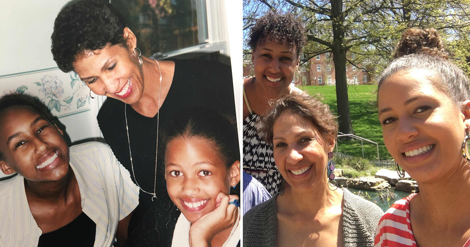 A woman with short curly hair smiles while standing over her two daughters who are also smiling and looking at the camera. Three women with dark tan skin and brown hair smiling on a sunny day with grass and trees in the background.