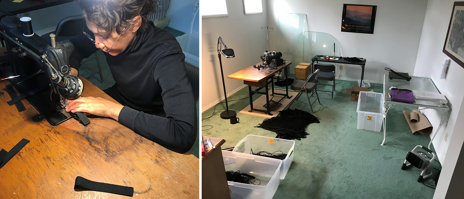 Woman in black long sleeve turtleneck with glasses sews loops with a black vintage sewing machine on a brown wood sewing table. A room with light green carpet and white walls with bins of equipment and workstation tables.