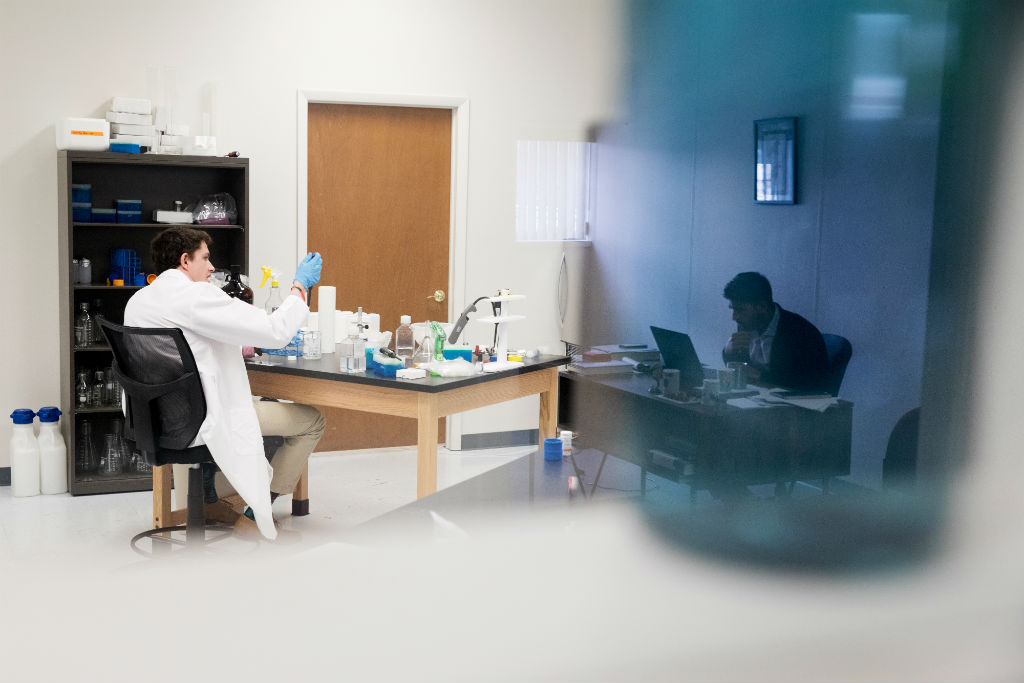 Joseph T. Frank conducts research in the lab as Ameer Shakeel, reflected in a water bottle, works across the hall on business needs.