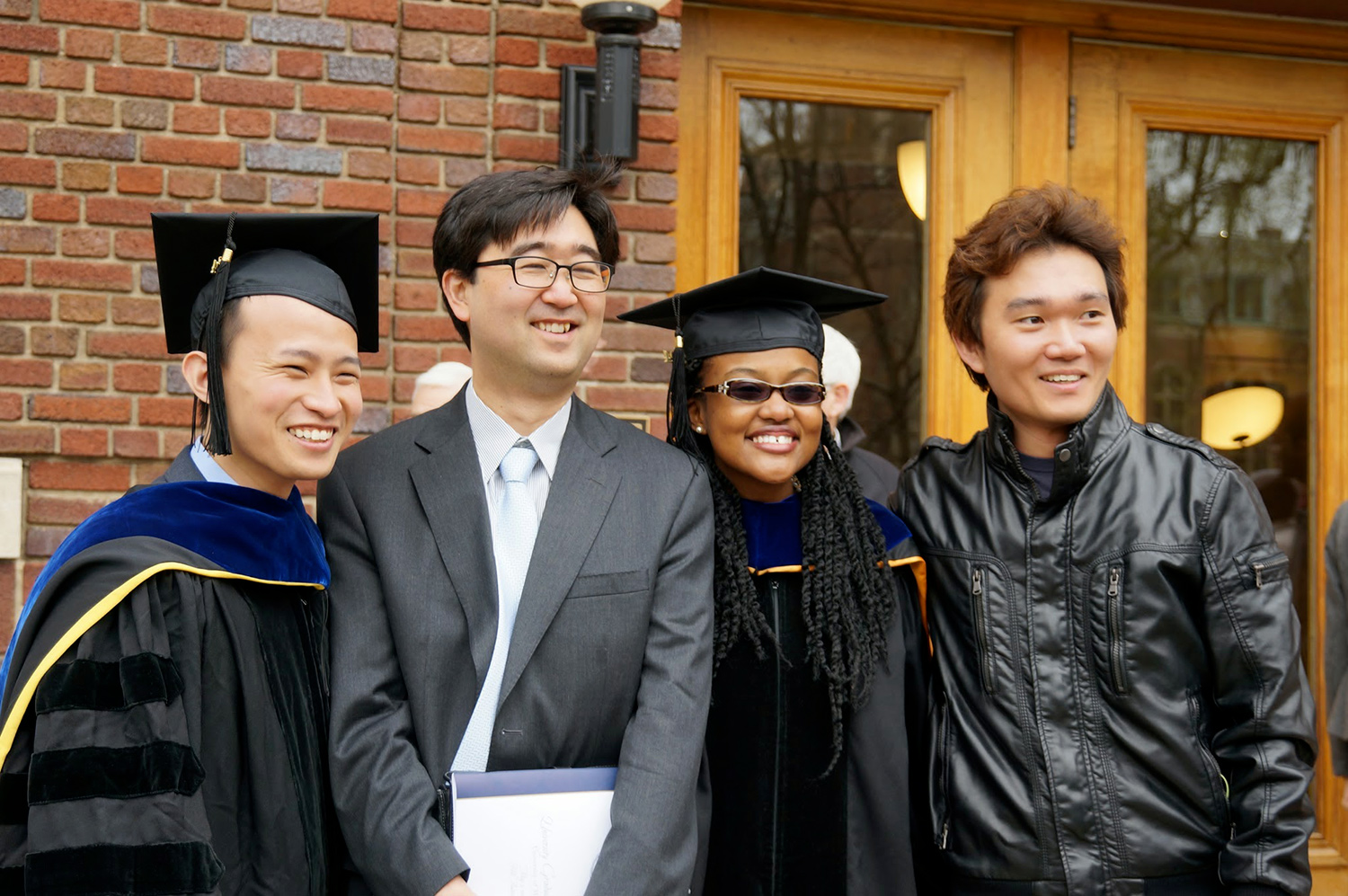 Arlyne Simon poses in her cap and gown with her advisor. Two male students frame them.