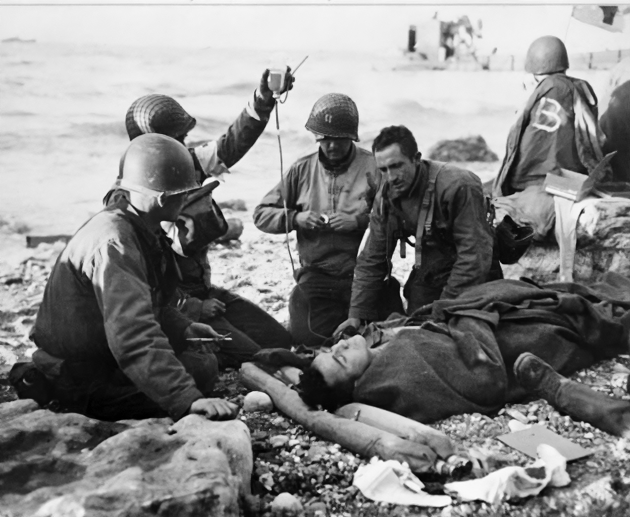 United States Army medical soldiers administer a plasma transfusion to an injured soldier on a beach in northern France during World War II. 