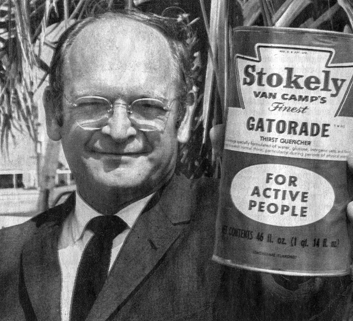 Man in a suit and glasses holds out a can of Gatorade