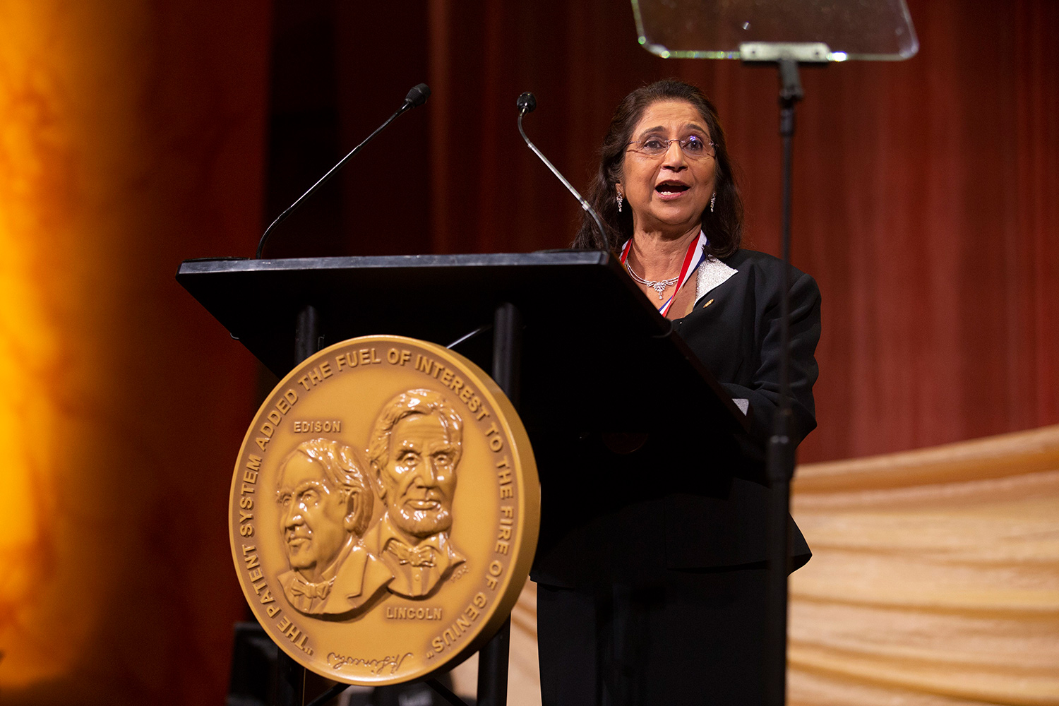 Woman wearing a black dress speaks from behind a podium during a ceremony.