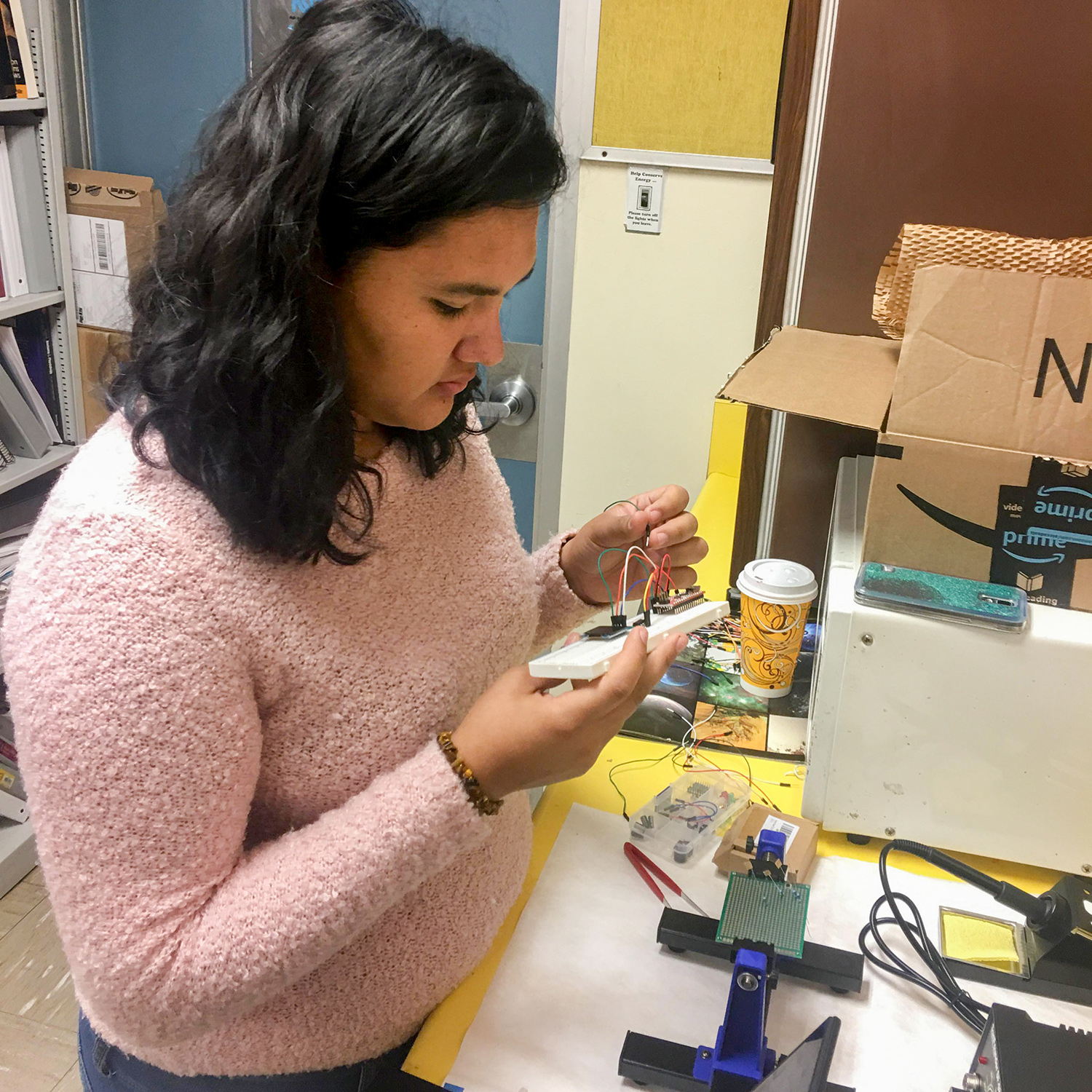 A young teenage girl, in a pink sweater, holds an electrical device in her hands.