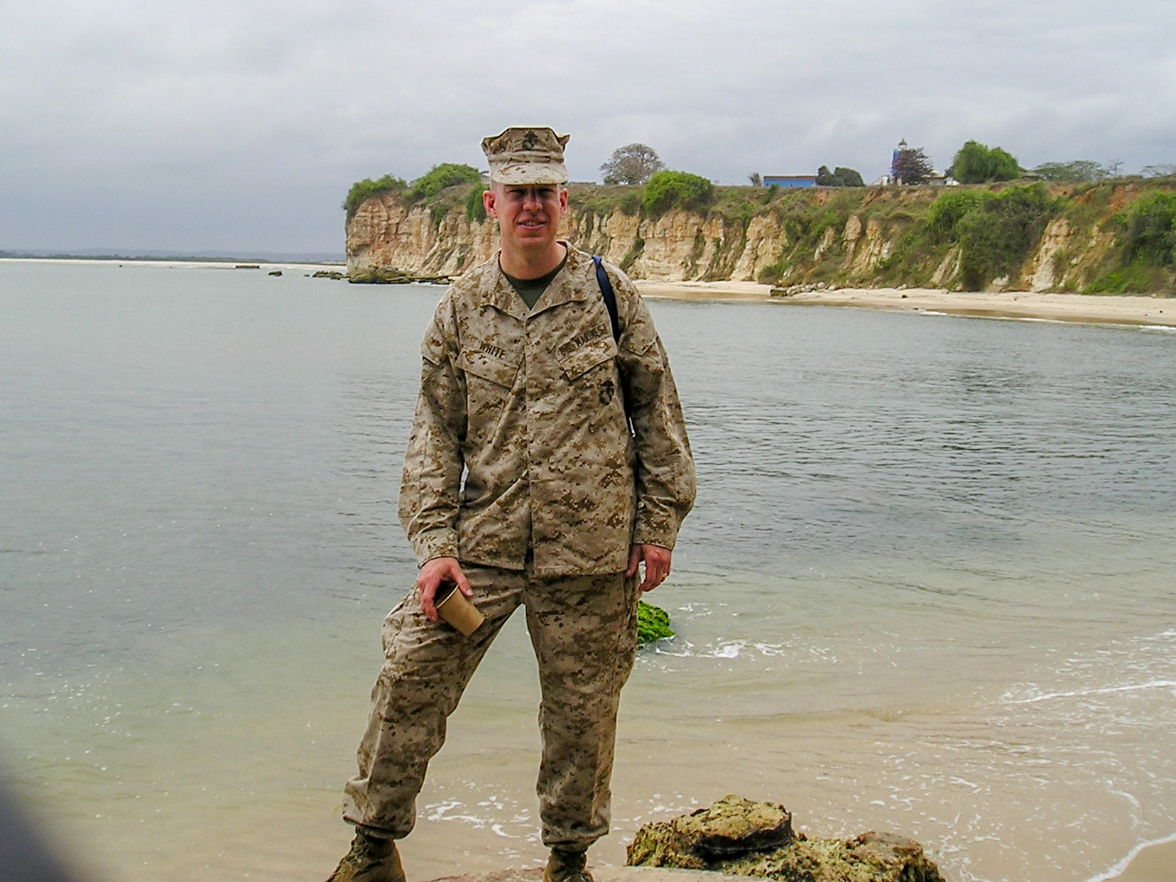 A man in a United States military uniform stands near the water’s edge.