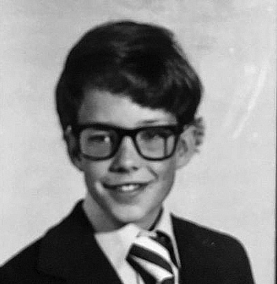  A black and white school photograph of an elementary-aged boy wearing black eyeglasses and a suit and tie outfit. 