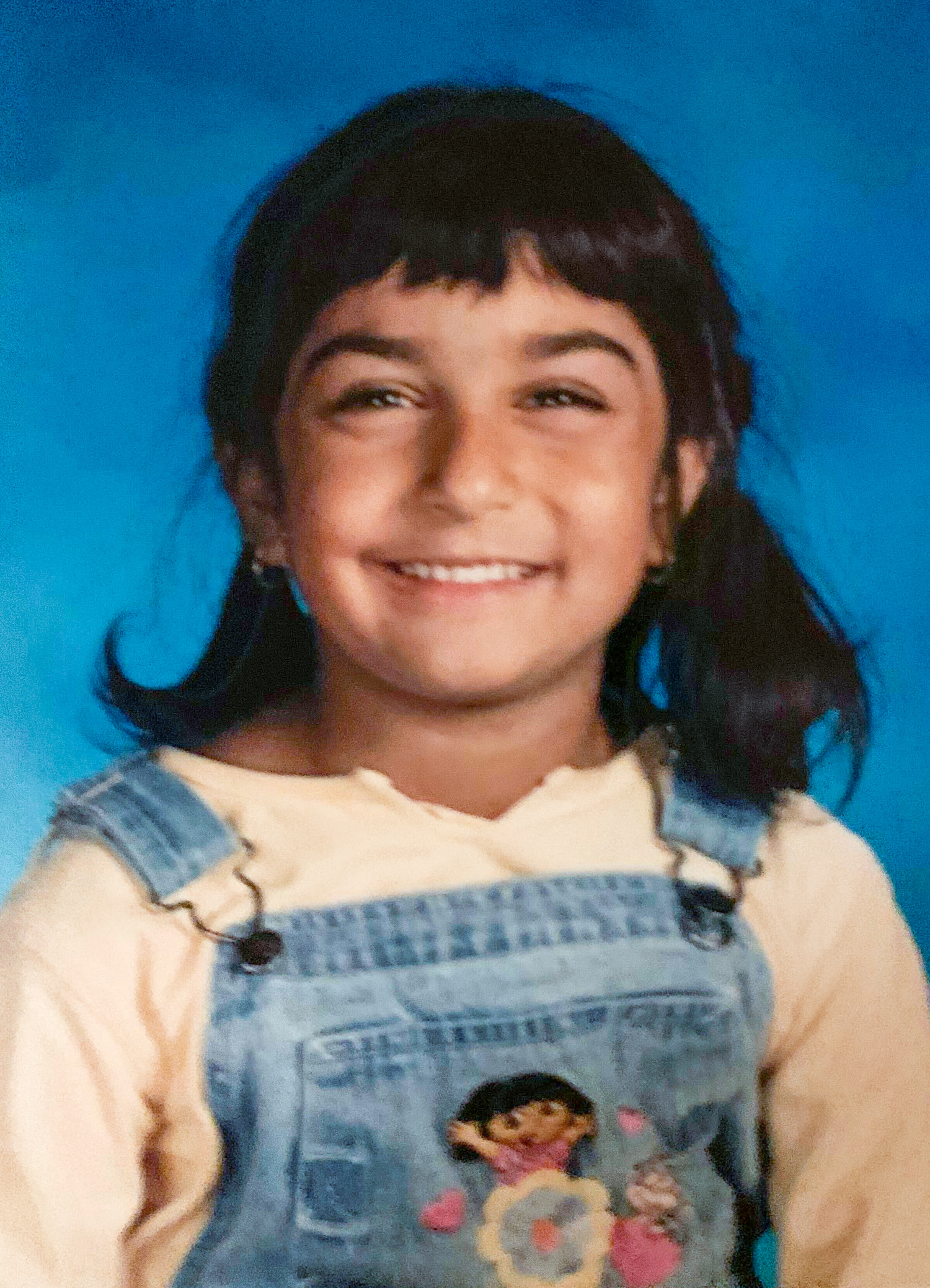 School photograph of young girl wearing a white shirt and overalls.