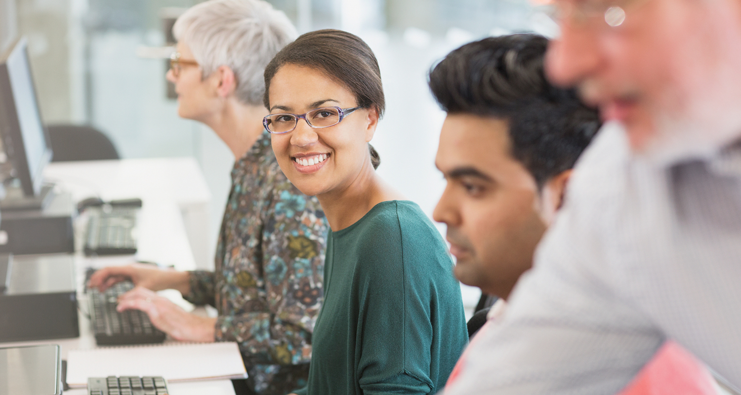 A group of people working at separate computers and one person looking up and smiling 