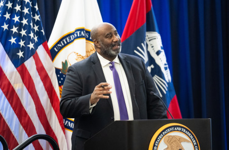 Acting Director Derrick Brent speaks from a USPTO podium at the agency's headquarters in Alexandria, Virginia, on January 15, 2025. In the background behind Brent are flags, including those of the United States and the USPTO.