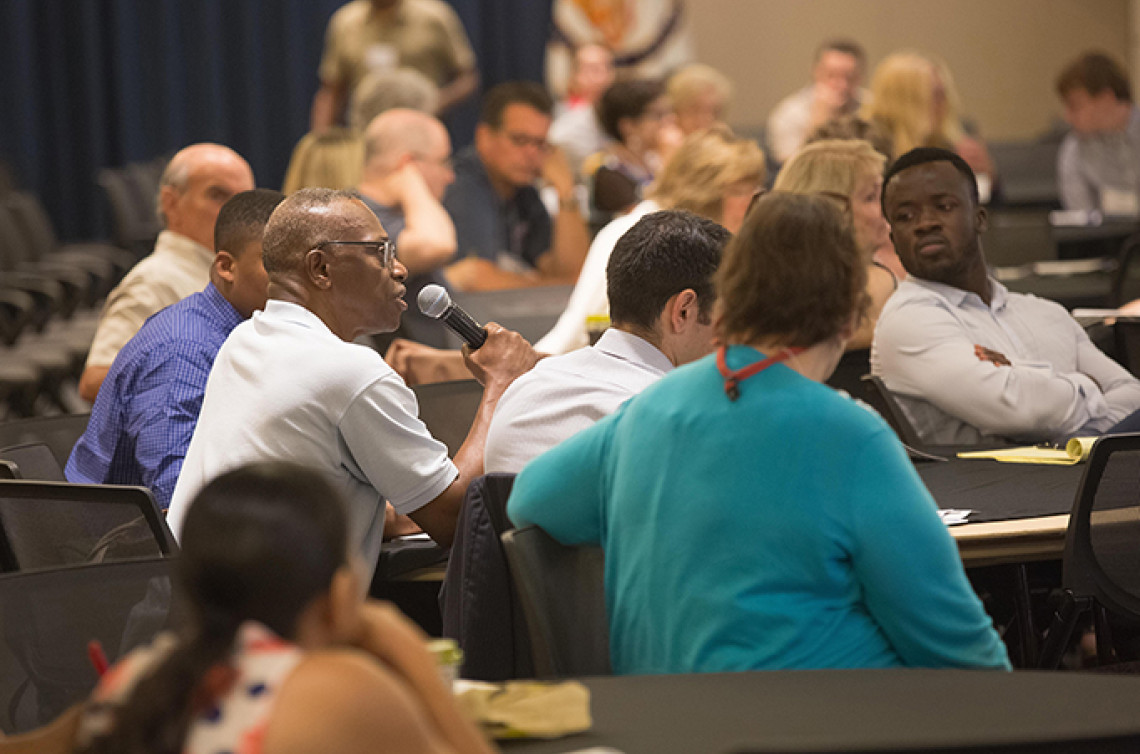 People sitting together listening to a person speaking through a microphone