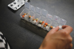 A hand organizes medical pills from their package into a weekly personal pill organizer