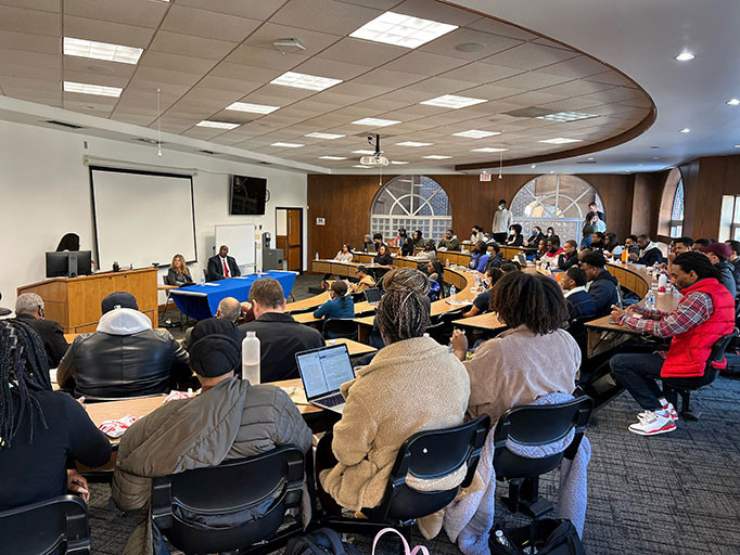 Director Kathi Vidal and Deputy Director Derrick Brent  sitting at a table in a lecture room filled with students 