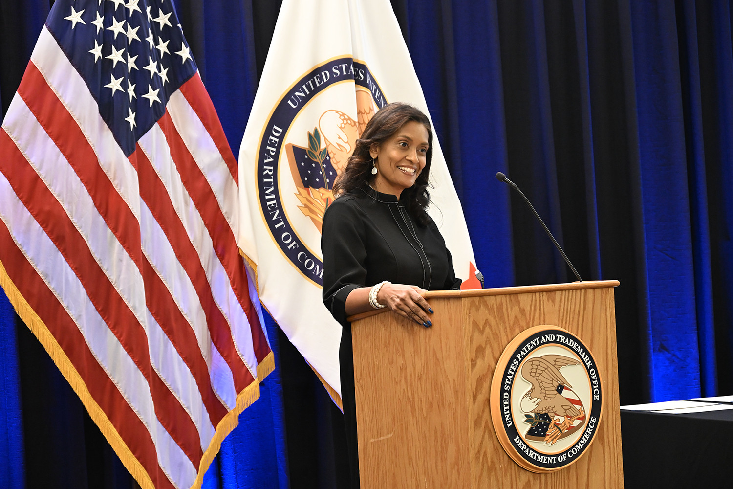 Commissioner for Patents Vaishali Udupa speaks from a USPTO podium to a ceremony of supervisory patent examiners on the agency's campus in Alexandria, Virginia, on November 12, 2024. Behind her are the flags of the United States and the USPTO.