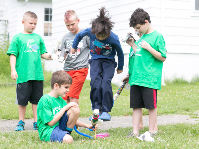 Several Camp Invention students gather outside to launch a bottle rocket. One holds the rocket while