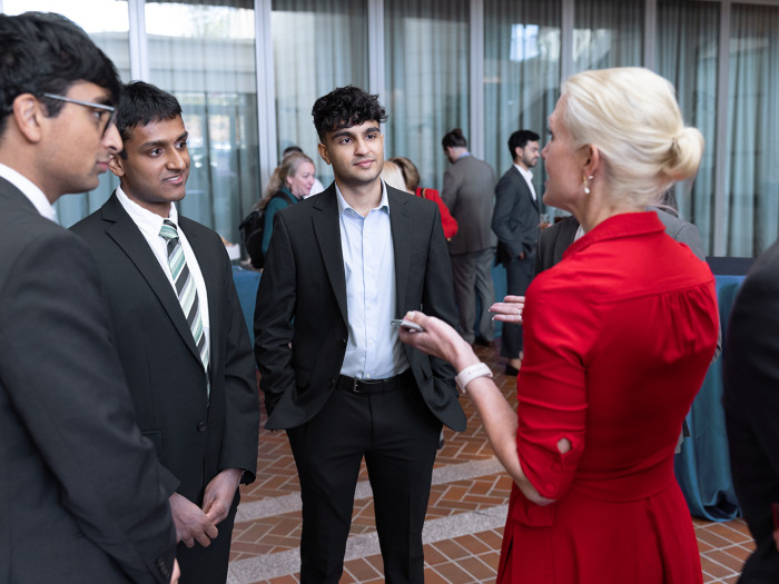 Three East Asian students stand in suits talking to a USPTO female employee who is wearing a red dre