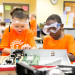 Two Camp Invention students wearing safety googles work on disassembling electronics.