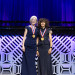 Two White female inventors in formal dresses stand on stage with their National Inventors Hall of Fa