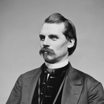 Man with short dark hair and mustache posing for a photograph wearing a 1850s-era suit.