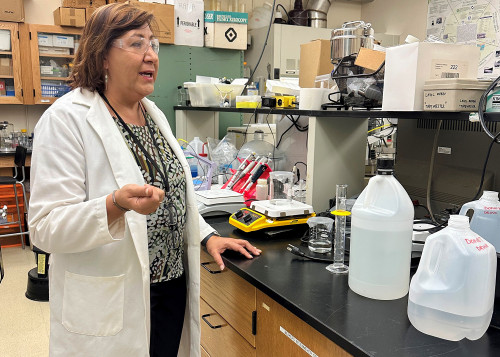 Chemist in lab coat and safety goggles surrounded by lab equipment