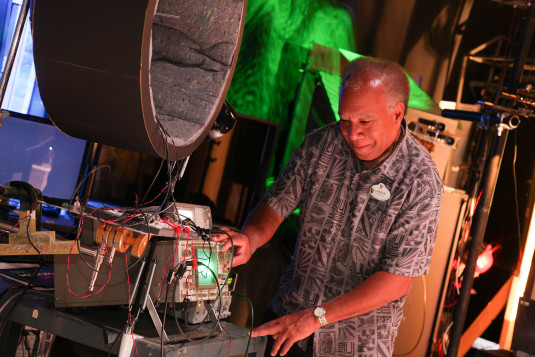 Lanny Smoot smiles while twisting a knob on a large machine as a Walt Disney Company employee