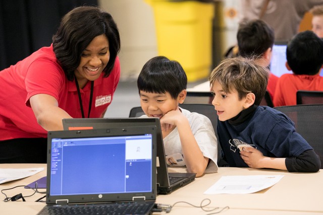 Smiling instructor works with two students on a project.