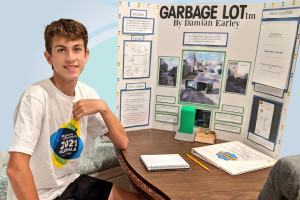 a male student sitting in front of a tri-fold poster.