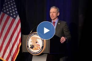 A man speaks behind a podium with the official USPTO seal, next to an American flag.