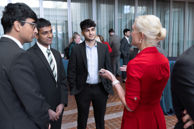 Three East Asian students stand in suits talking to a USPTO female employee who is wearing a red dress.