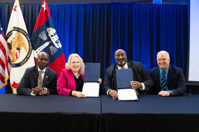 Harold Ross, Doreen Greenwald, Derrick Brent, and Fred Steckler seated at a table and displaying the signed Collective Bargaining Agreement. 