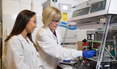 Two females in lab coats examining equipment in a lab.