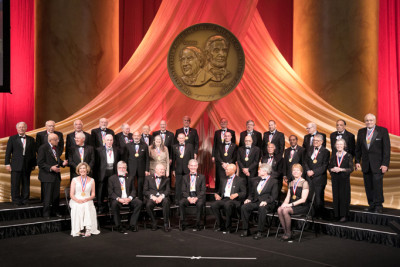 Men and women in black tie attire being honored on-stage under.