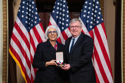 Eric R. Fossum and White House Office of Science and Technology Policy Director Arati Prabhakar smile and show a medal.