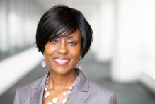 Headshot of USPTO Patent Attorney Carmen L. She wears a light gray pin-stripe blazer and multi-strand pink and white necklace with matching earrings and is smiling.