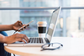 Person working on laptop and holding phone