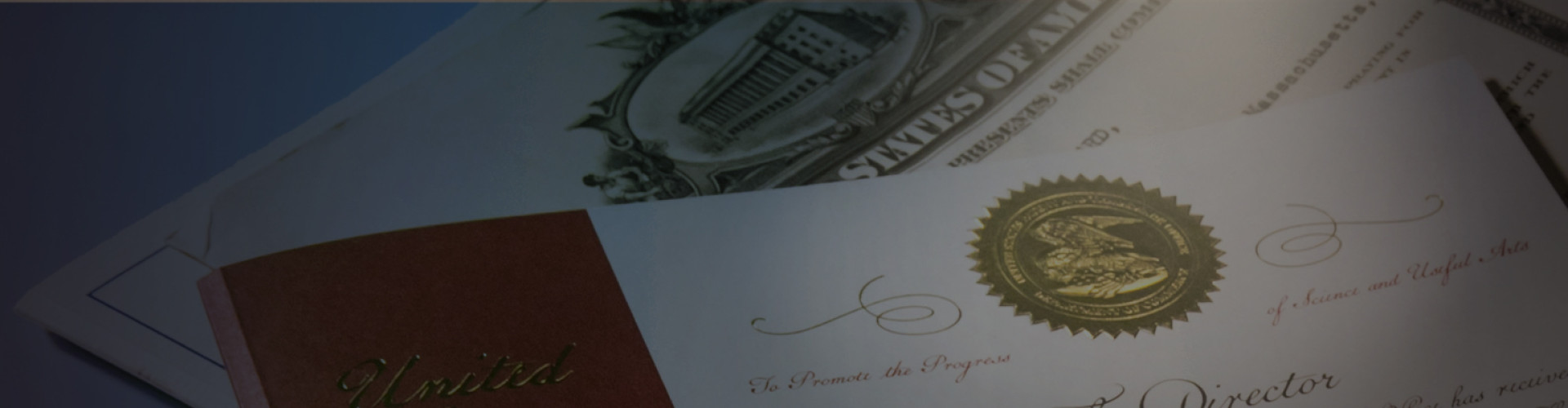This photo shows a US Patent certificate. The photo is dark and there is spotlight pointed at the gold-colored seal that is located at the top of the certificate.