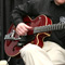 Photo of a man sitting in a chair playing a red guitar.